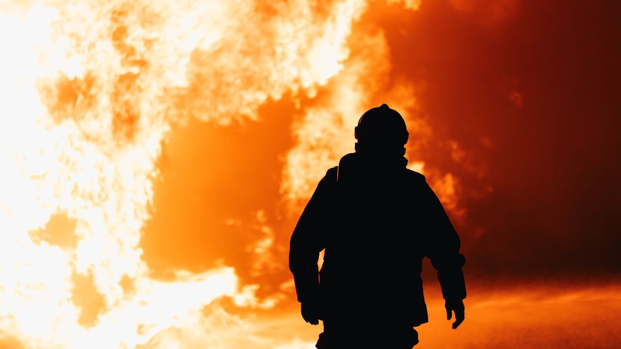 About Silhouette of a firefighter standing against a massive fire, capturing the bravery and intensity of the scene.